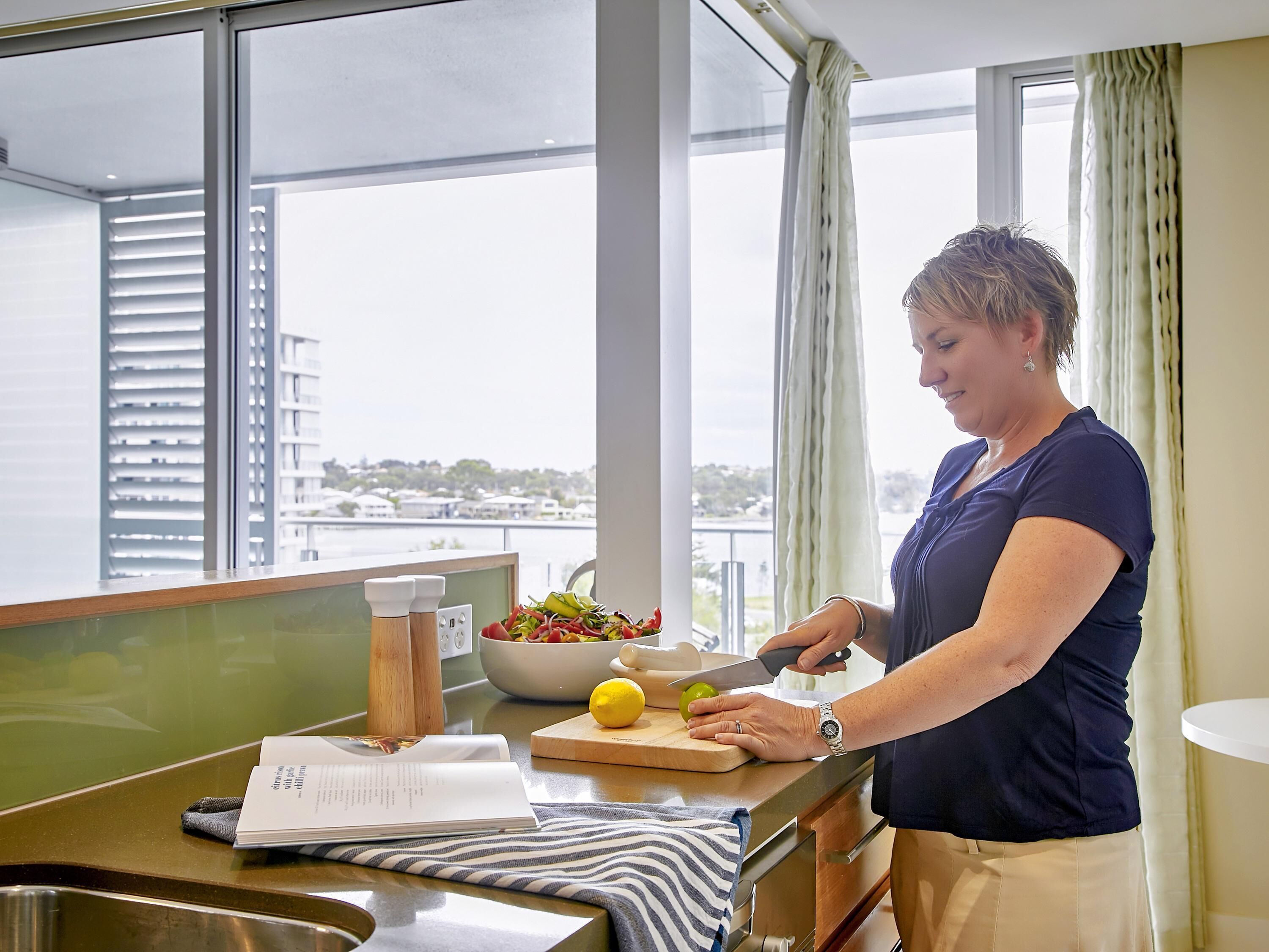 Una persona preparando comida en una cocina con vistas a un paisaje urbano a través de amplios ventanales.