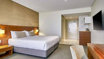 A modern hotel room with a large bed, bedside tables, a desk, and a TV.