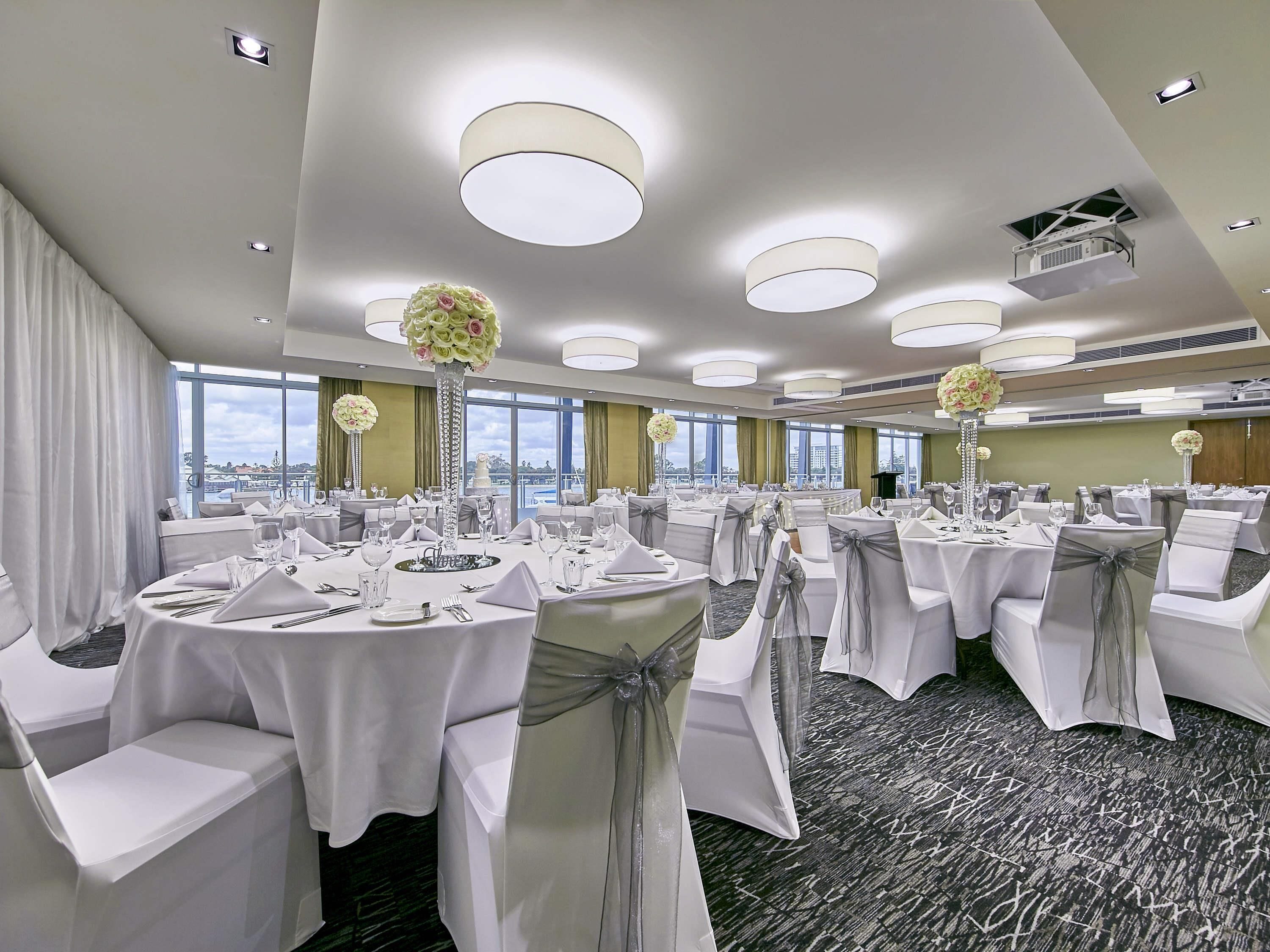 A banquet hall with round tables, white tablecloths, and chairs with sashes.