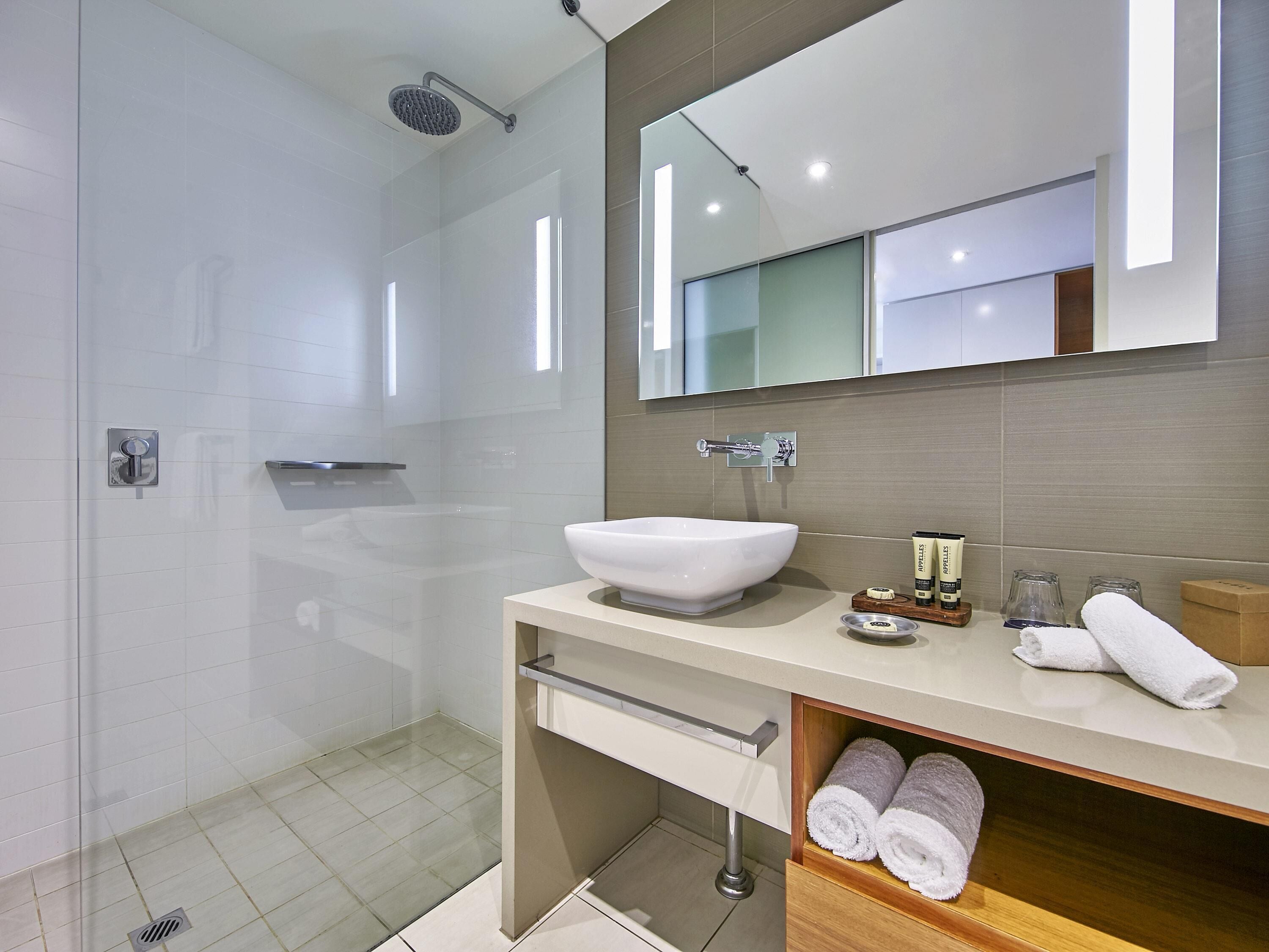 Un bagno moderno con un ampio specchio, un lavandino bianco e una cabina doccia.