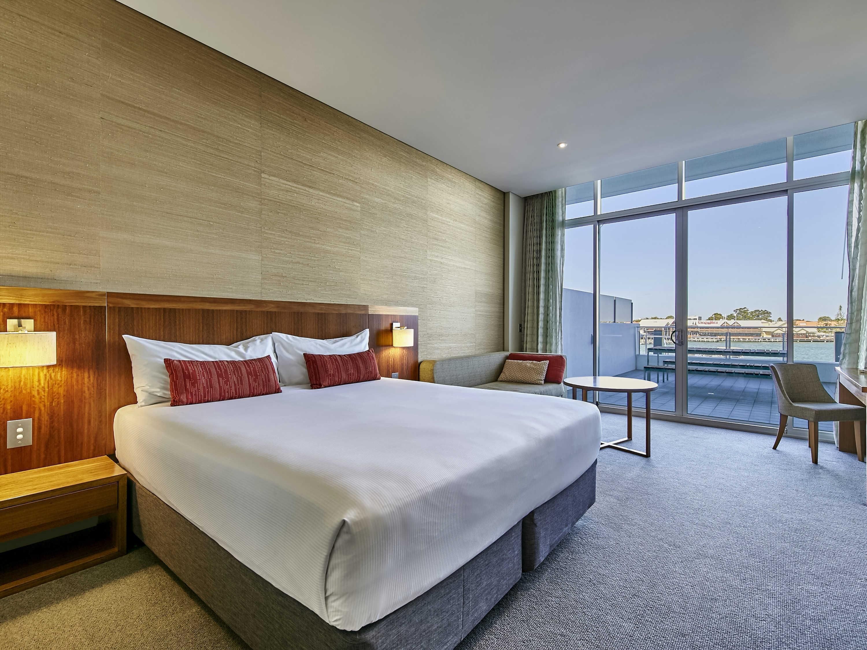 A hotel room with a large bed, a small sofa, a table, and a view of the water.