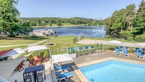 A pool area with lounge chairs and umbrellas, a wooden deck, and a view of a lake and forest. - VVF Corrèze Pays d'Eygurande (Eygurande)