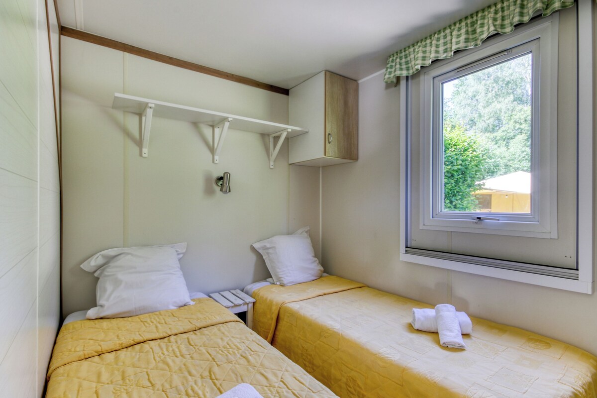 A room with two beds, a window with a view, a shelf, and a cabinet.