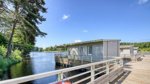 A wooden dock extending over a calm river, with a small building and a lifebuoy visible. - VVF Corrèze Pays d'Eygurande (Eygurande)