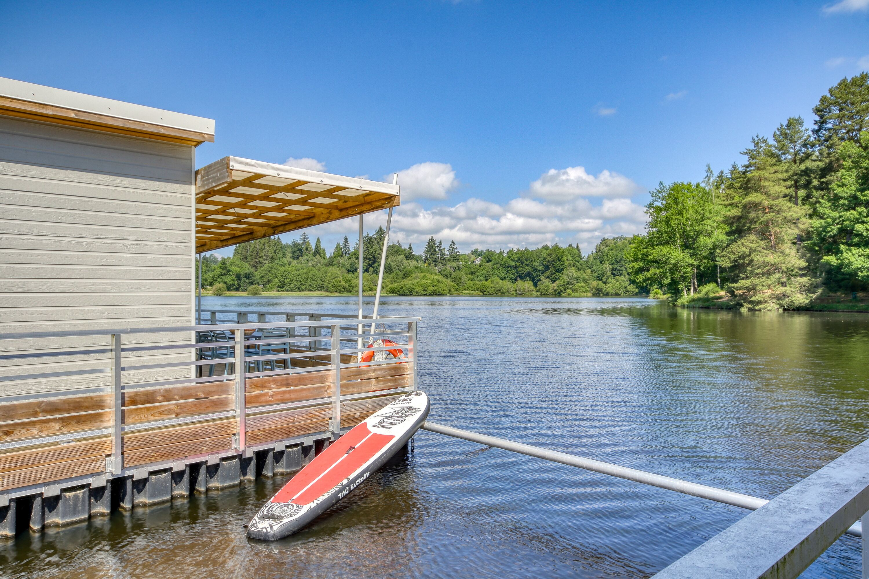 A dock with a paddleboard, a wooden deck, and a building with a covered area.