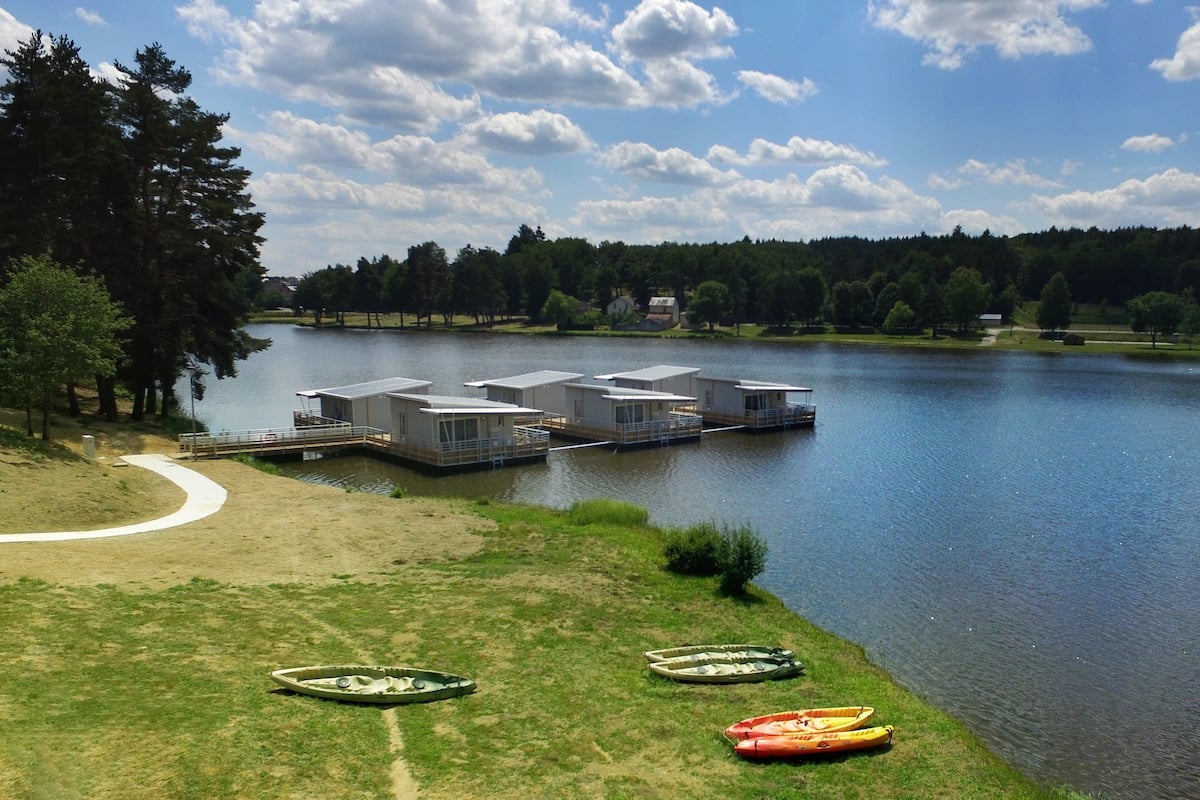 Ein Seeufergrundstück mit schwimmenden Häusern, die durch Wege miteinander verbunden sind, einer Rasenfläche mit Kajaks und einem klaren Himmel.