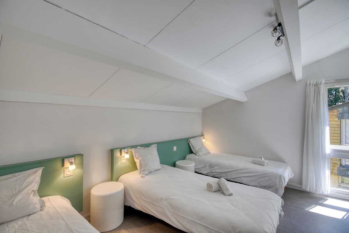 Ein Zimmer mit zwei Betten, einem kleinen runden Tisch und einem Fenster mit Vorhängen.