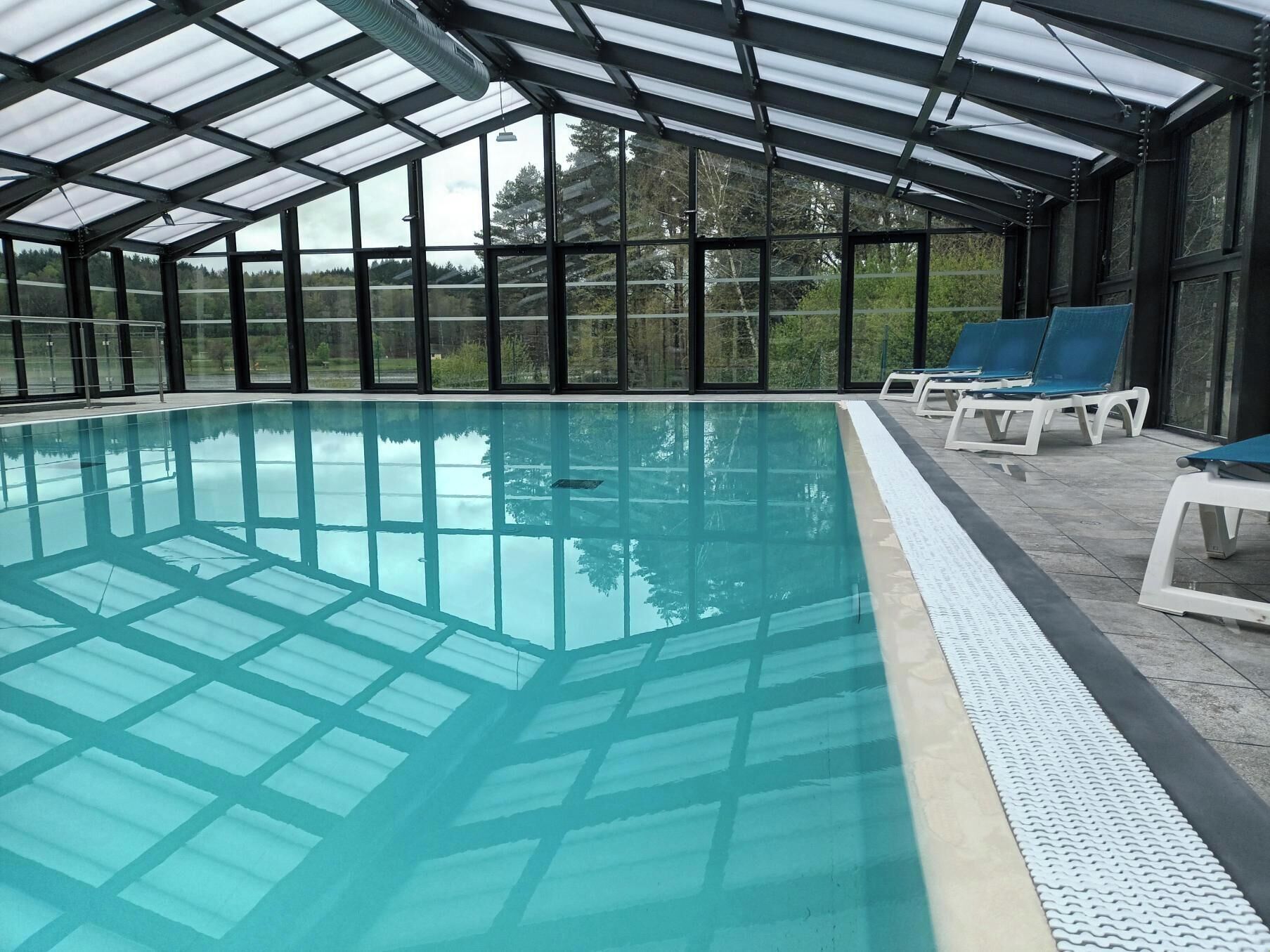Une piscine intérieure dotée de panneaux de verre transparent et d’une terrasse carrelée.