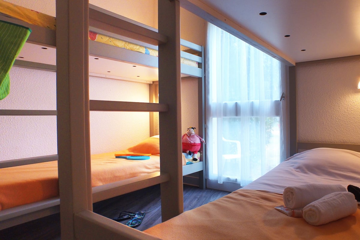 A hotel room with bunk beds, a window with curtains, a bedside lamp, and a teddy bear on the bed.