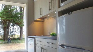 Une cuisine moderne dotée d’un lave-vaisselle encastré, d’appareils électroménagers en acier inoxydable et offrant une vue sur une forêt grâce à une grande fenêtre.