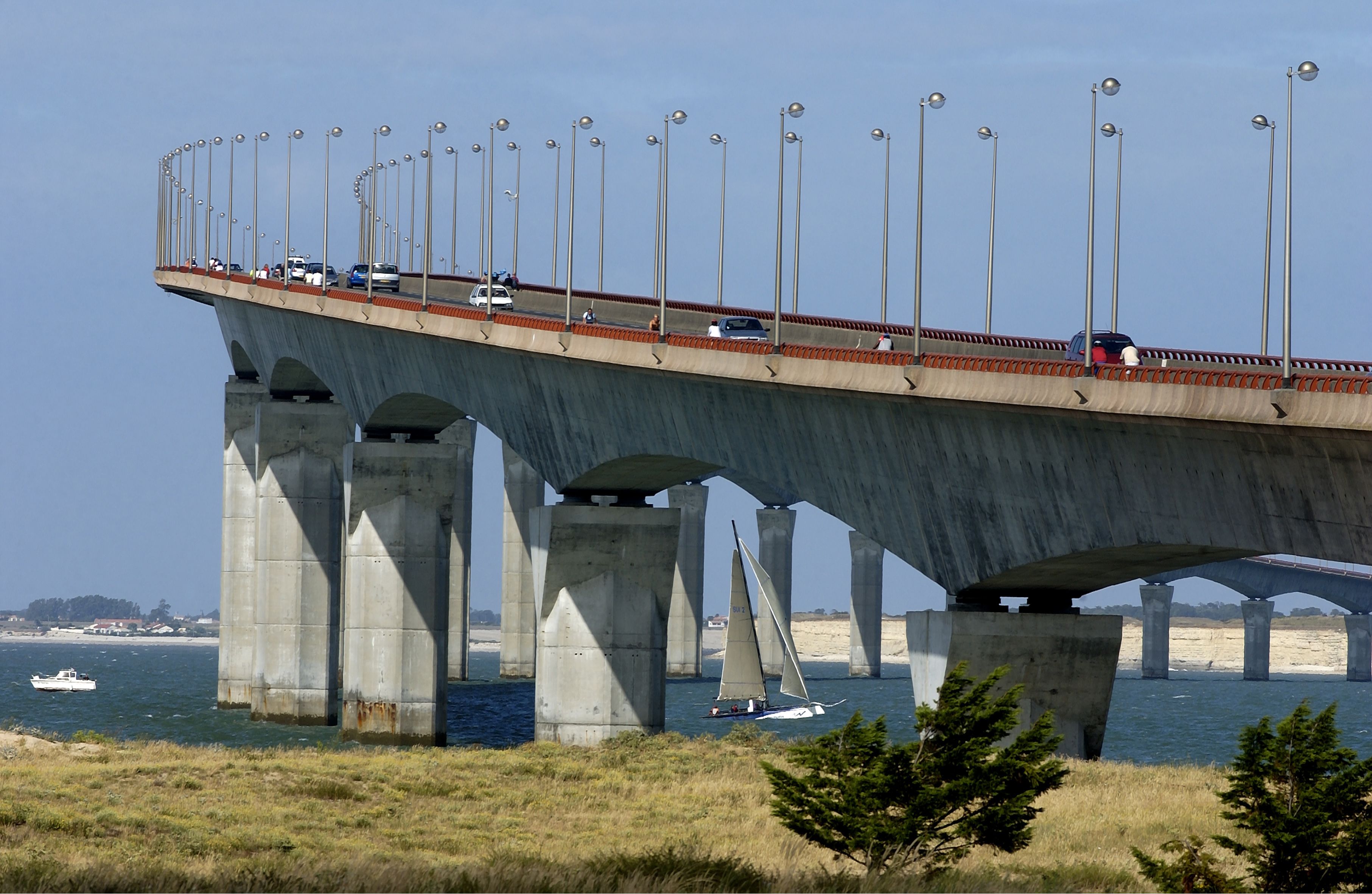 Un puente con varios carriles de tráfico y un velero en el agua.