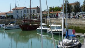 Un port de plaisance avec plusieurs bateaux amarrés, un mur de pierre et des bâtiments en arrière-plan.