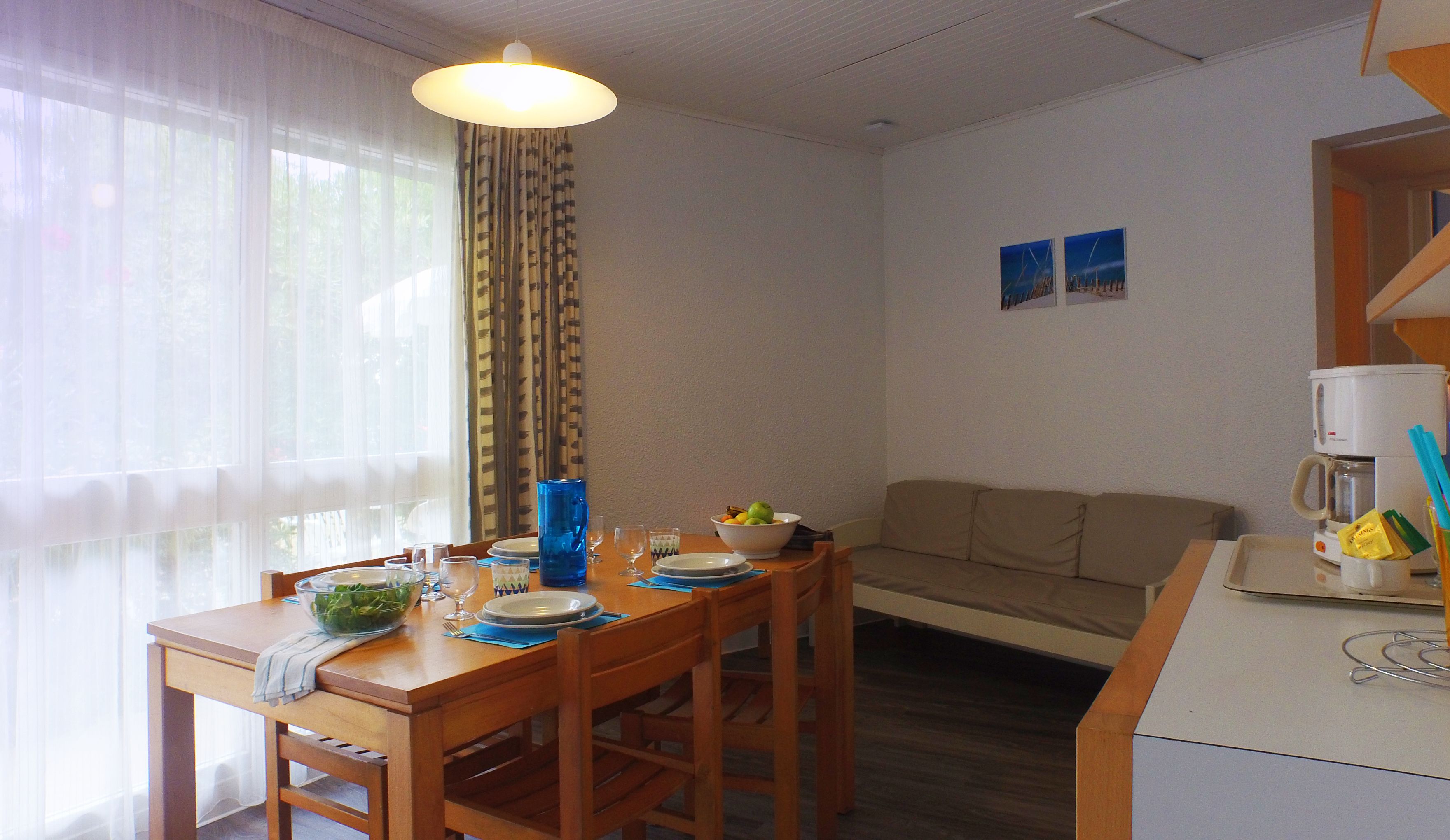 A dining area with a table set for two, a bowl of salad, and a coffee maker on the counter.