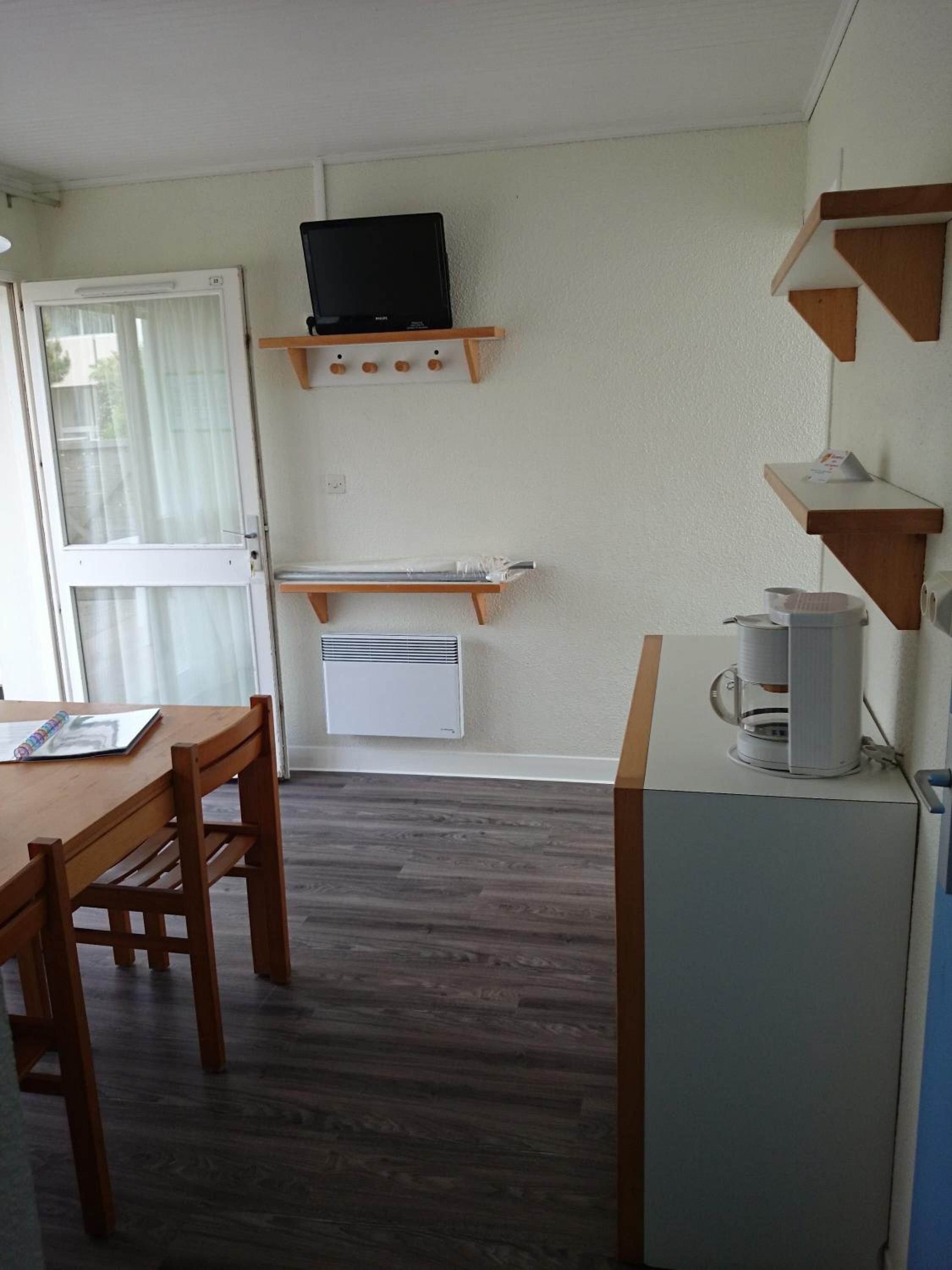 A compact kitchen with a wooden table and chairs, a built-in TV, and a coffee machine.