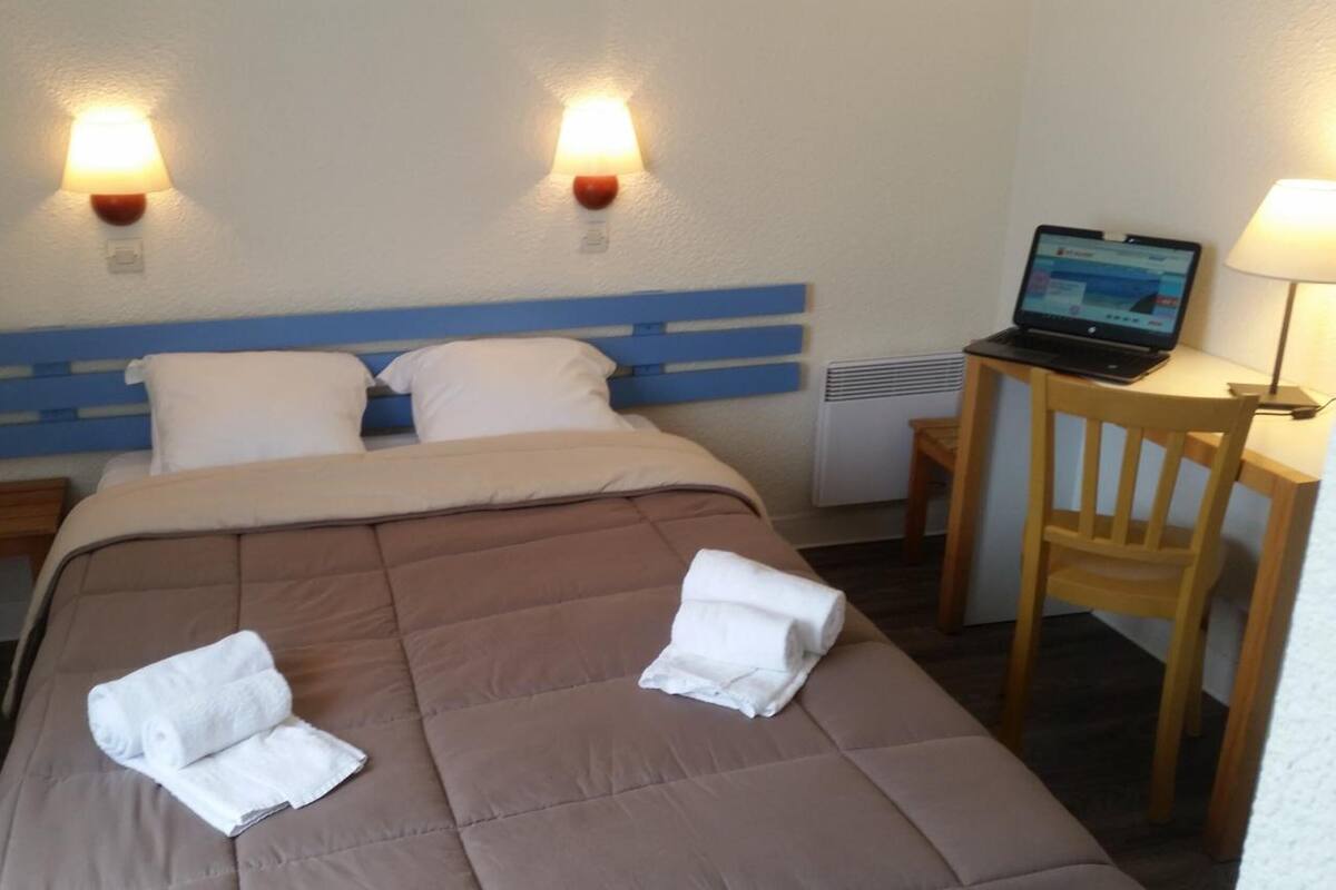 A hotel room with a bed, two bedside lamps, a laptop on a desk, and a chair.