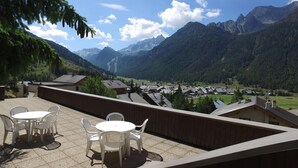 A terrace with a view of a mountain village, wooden deck, and white plastic chairs. - VVF Queyras, Ceillac-en-Queyras (Ceillac)