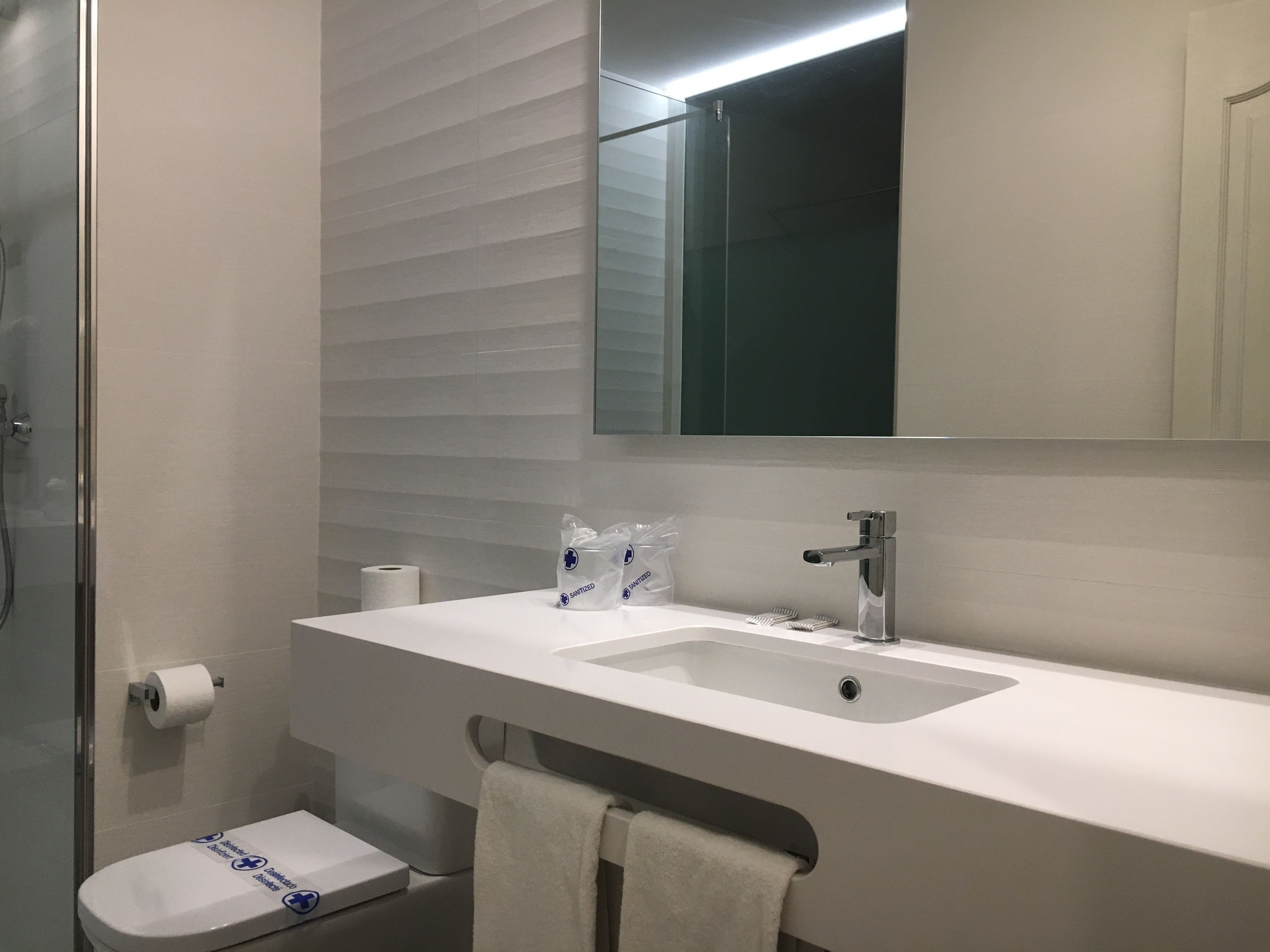 Une salle de bain moderne avec une douche à l’italienne en verre, un lavabo blanc avec un miroir au-dessus et des toilettes avec une serviette accrochée au mur.
