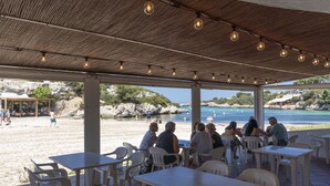 Un área de estar al aire libre con mesas y sillas, con vista a una playa y al mar.