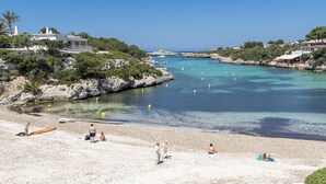 Escena de playa costera con aguas cristalinas, afloramientos rocosos y algunas personas disfrutando de la playa.