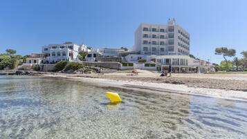 A coastal hotel with multiple buildings, clear waters, and a sandy beach.