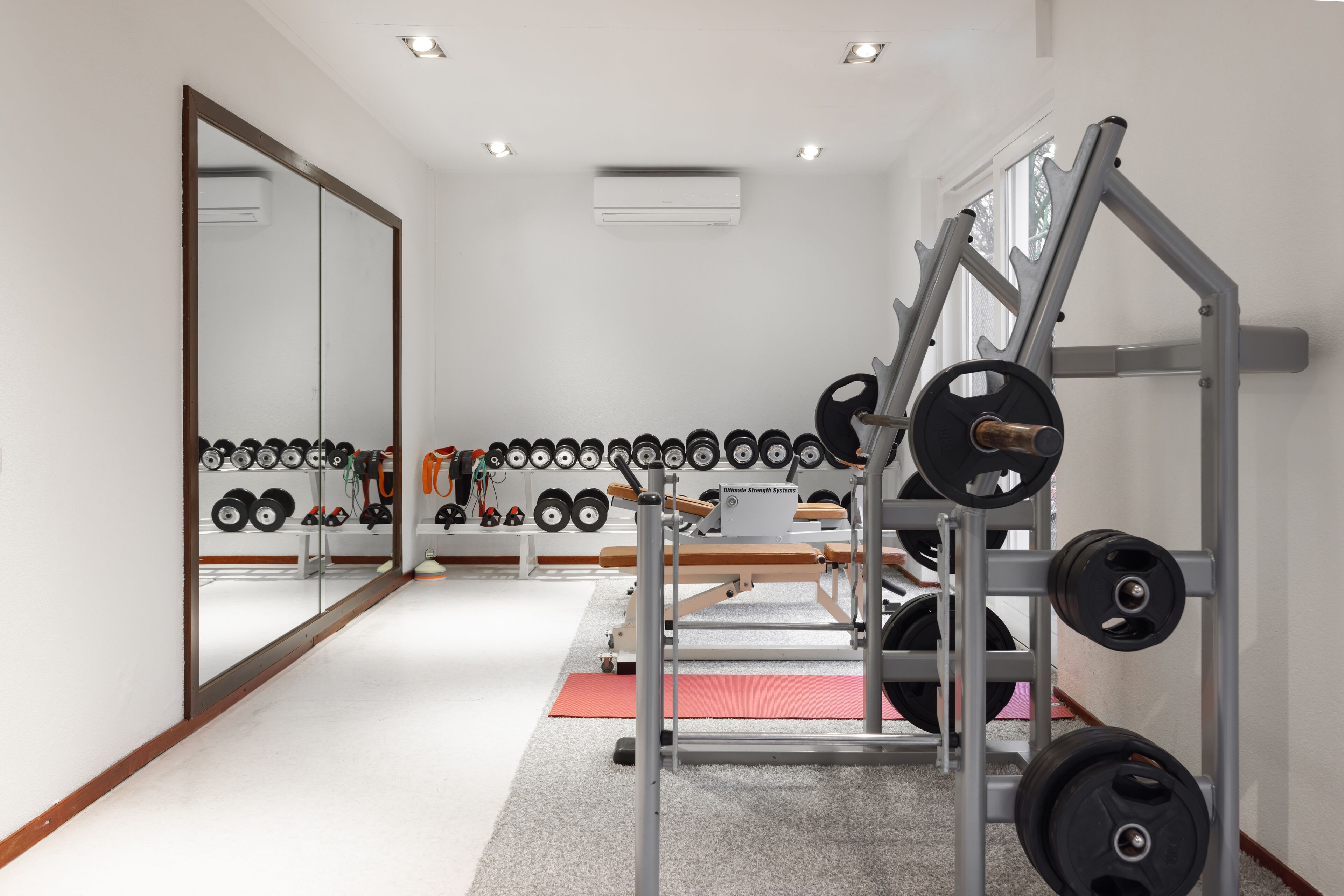Un gimnasio con equipo de levantamiento de pesas, un espejo grande y una hilera de mancuernas.