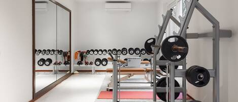 Un gimnasio con equipo de levantamiento de pesas, un espejo grande y una hilera de mancuernas.