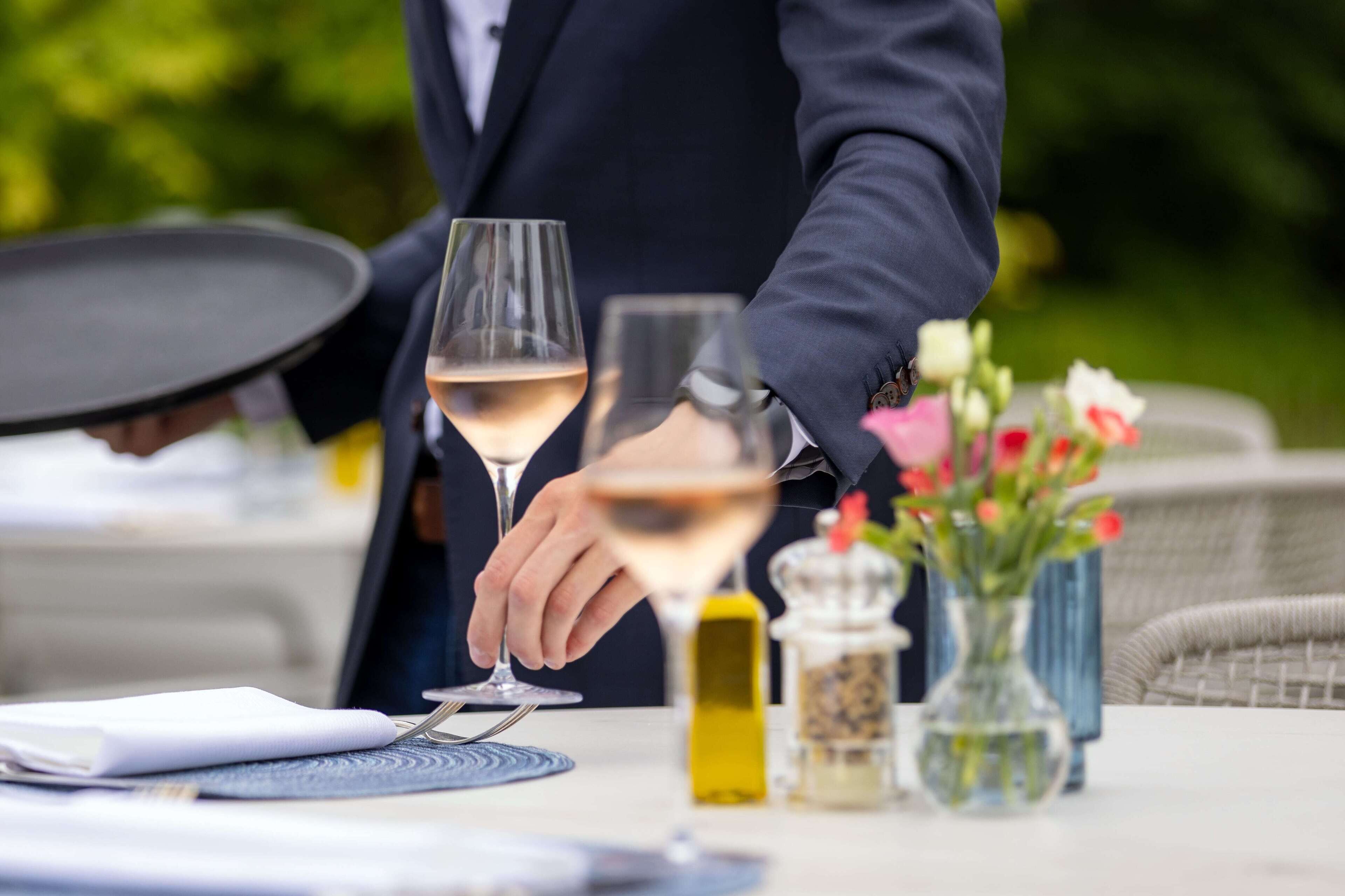 A dining table with a wine glass, a bottle of olive oil, and a vase with flowers.