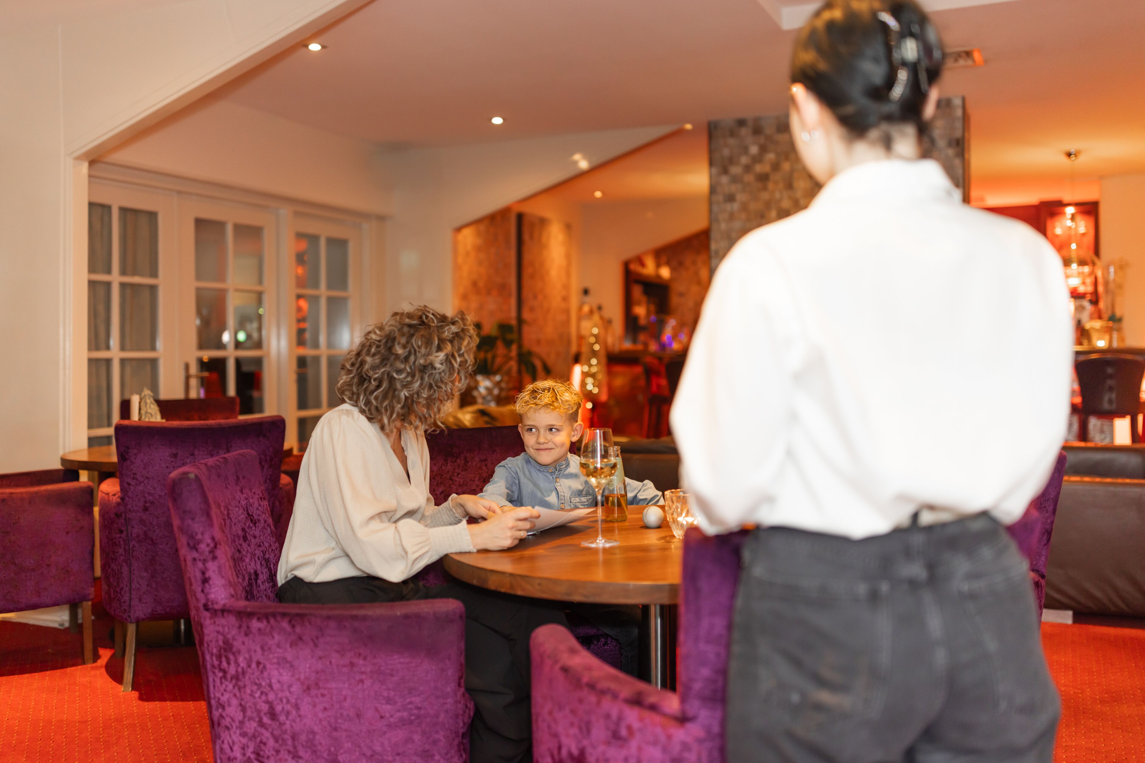 A dining area with purple velvet chairs, a round table, and a person seated at the table.