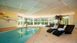 Piscina interior con sillas de descanso y un amplio ventanal con vistas a zonas verdes.