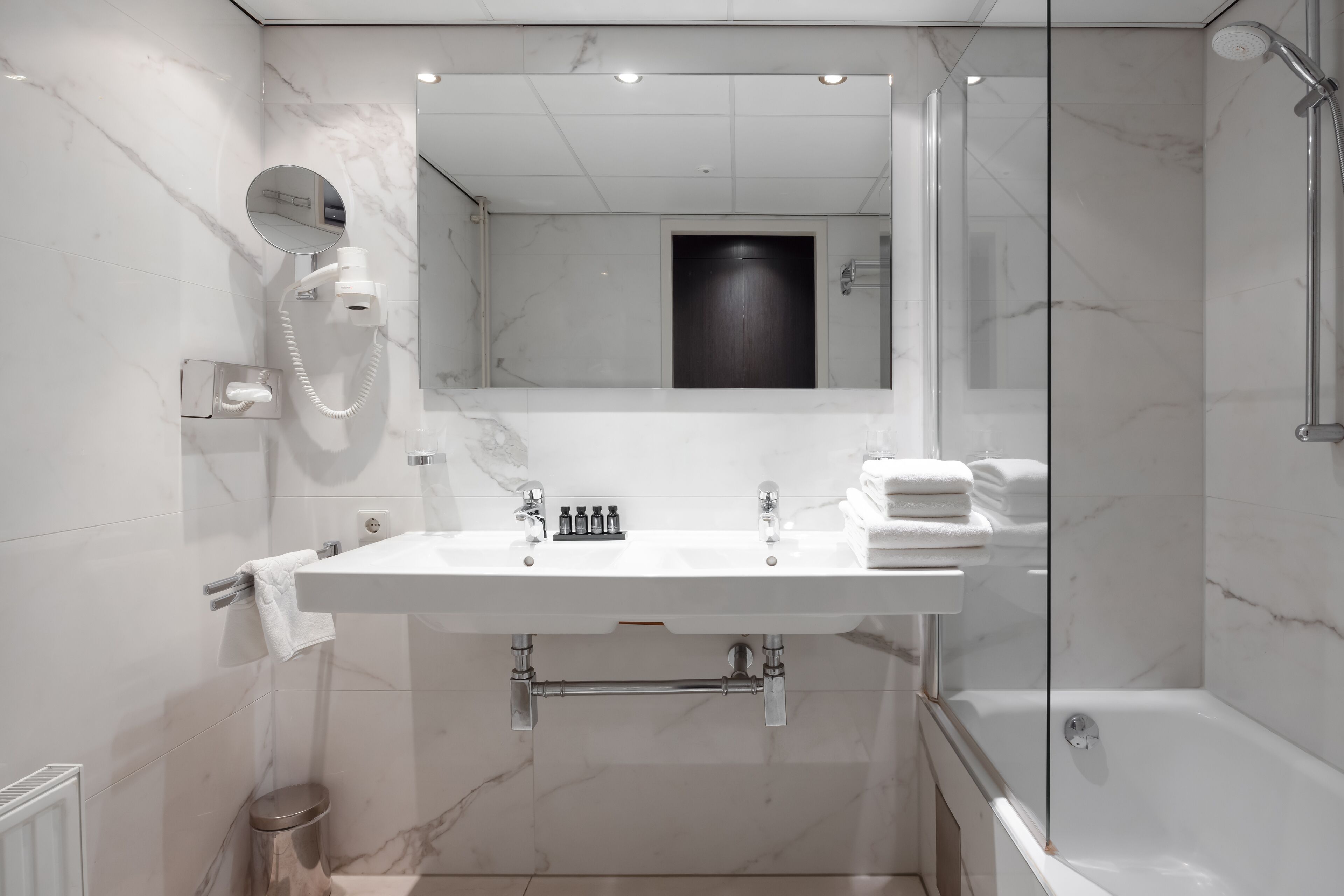 Une salle de bain moderne avec un grand miroir, un lavabo blanc, une douche et des toilettes.