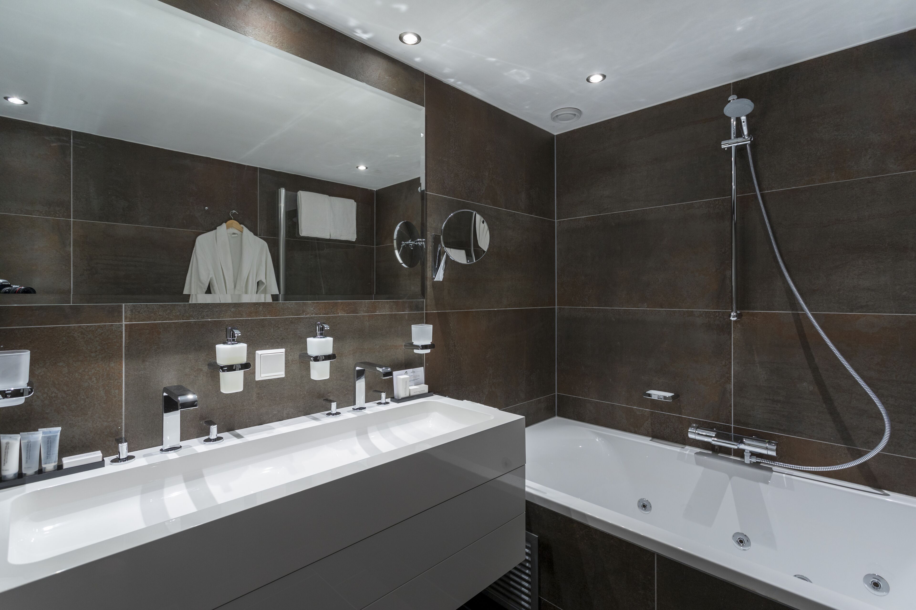 Un baño moderno con tocador doble lavamanos, un espejo grande, cabezal de ducha de mano y una bañera independiente.