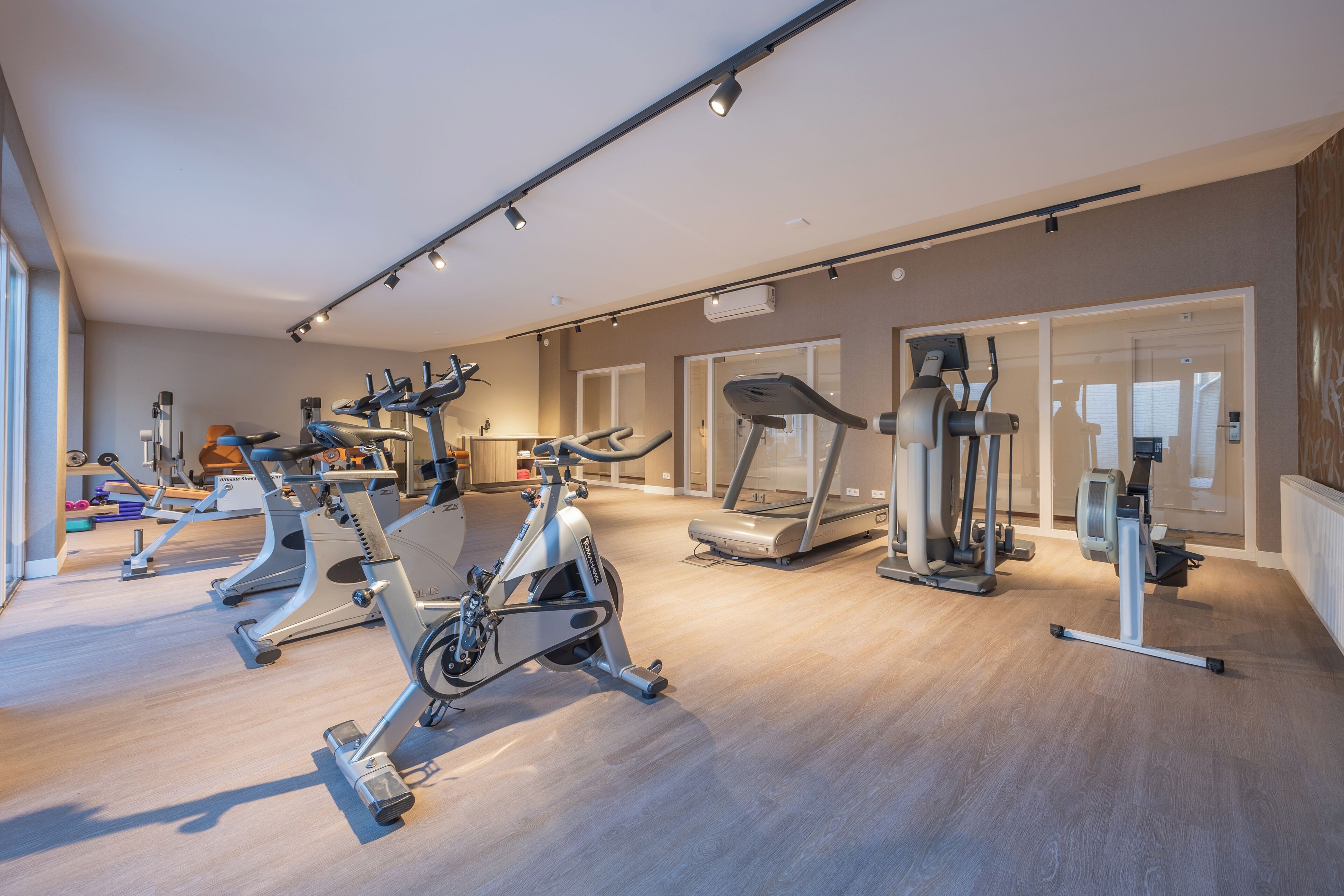 Ein modernes Fitnessstudio mit verschiedenen Cardio-Geräten, einer Gewichtbank und einem Spiegel.