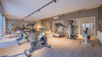 A modern gym with various cardio machines, a weight bench, and a mirror.