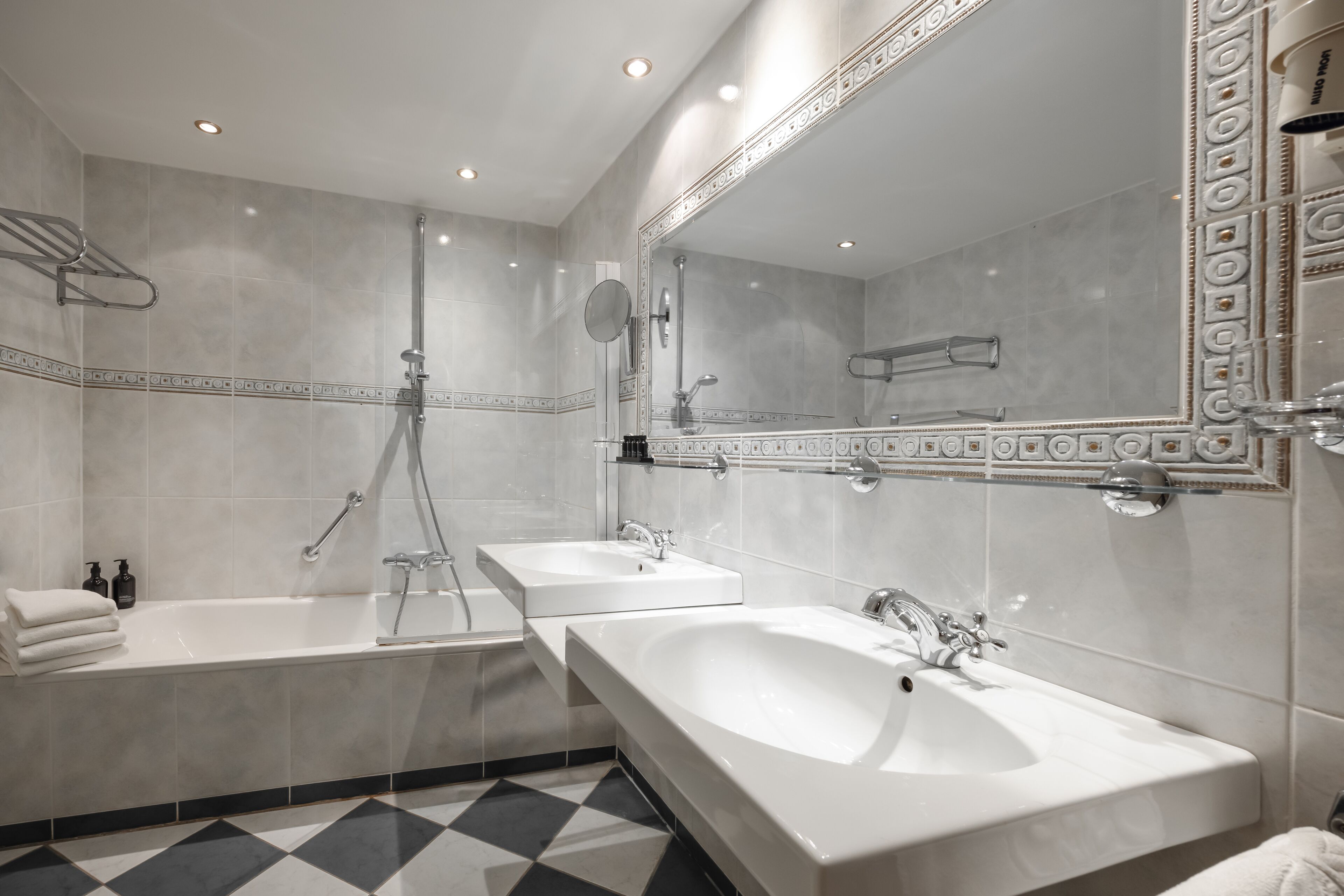 A modern bathroom with two sinks, a bathtub, and a large mirror.