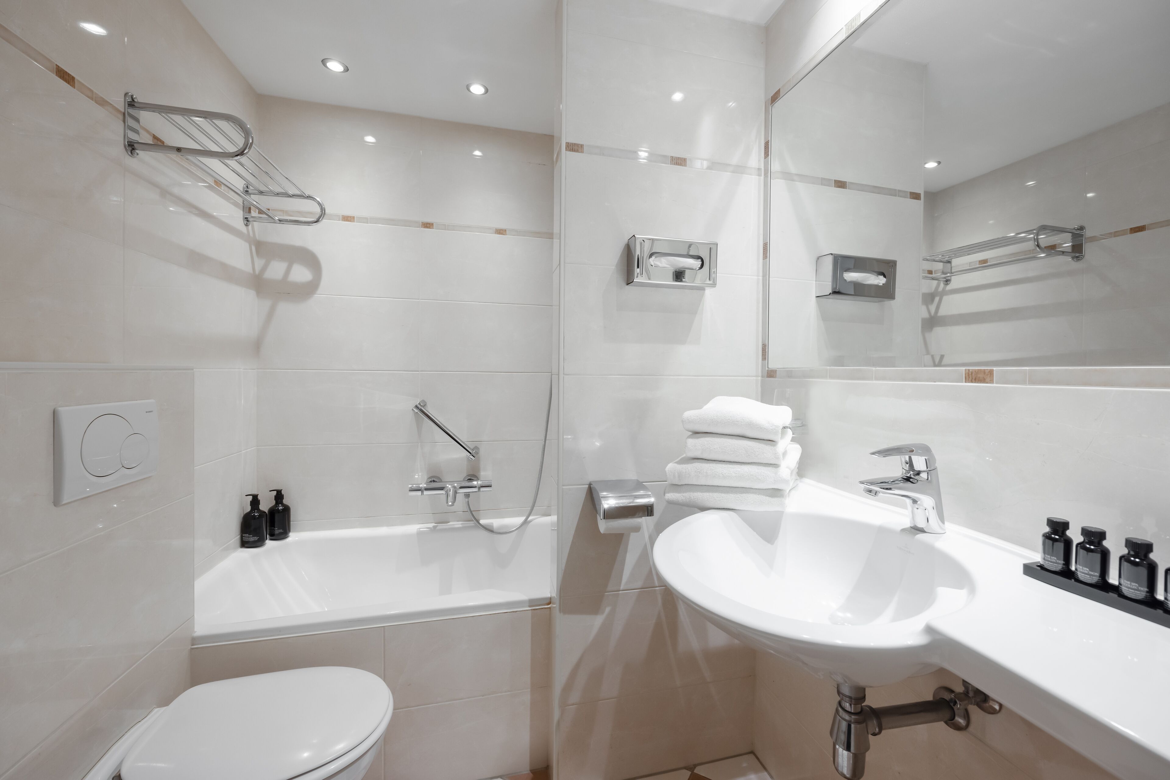 A modern bathroom with a white toilet, a bathtub, a sink, and a mirror.