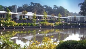 Un hotel con un cuerpo de agua reflectante en primer plano, rodeado de vegetación y árboles.