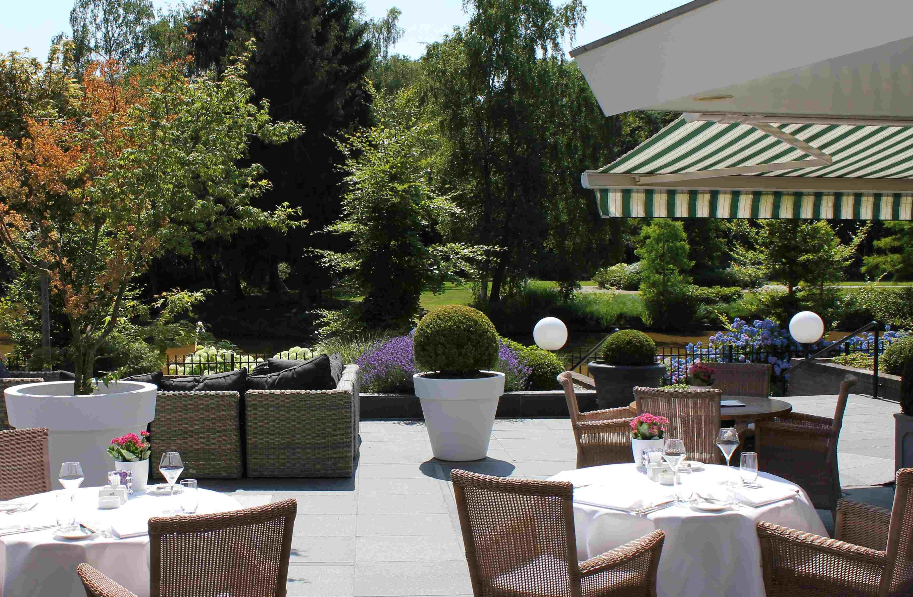 An outdoor dining area with wicker furniture, white tablecloths, and potted plants.