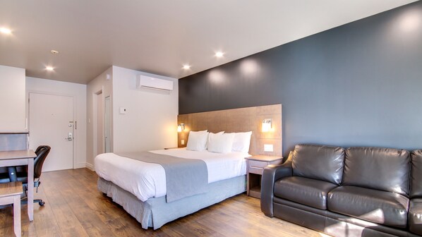 A hotel room with a bed, a desk, a chair, a leather sofa, and a wall-mounted light fixture.