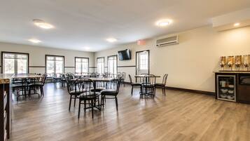 A spacious dining area with multiple tables and chairs, an air conditioning unit, and a television mounted on the wall.