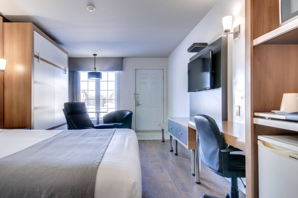 Una habitación de hotel con una cama grande, un escritorio con una silla, una televisión y una ventana con cortinas.