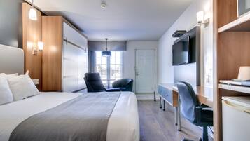 Una habitación de hotel con una cama grande, un escritorio con una silla, una televisión y una ventana con cortinas.