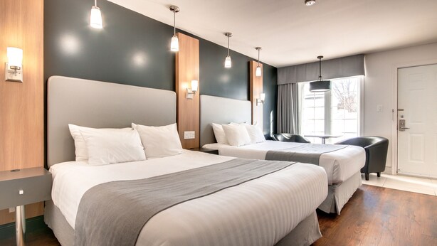 A hotel room with two beds, a wooden headboard, a bedside table, and a window with curtains.