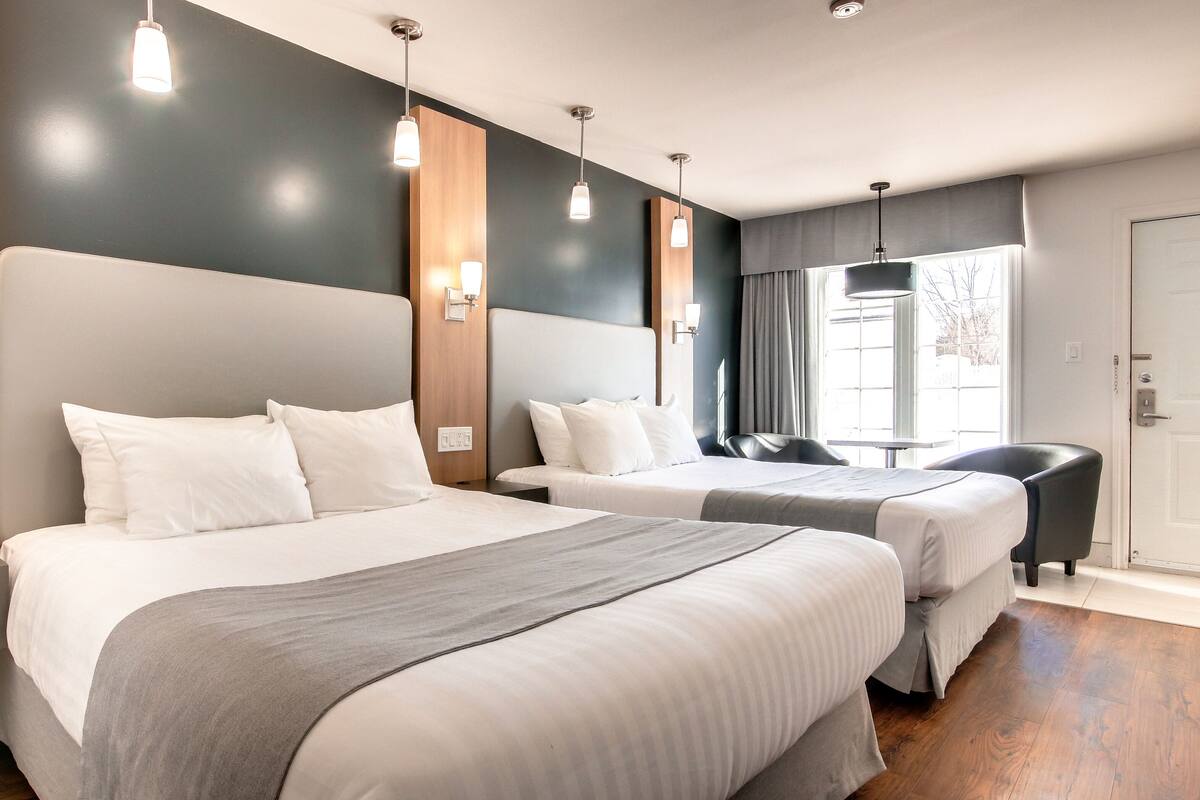 Habitación de hotel con dos camas, cabecero de madera, mesita de noche y ventana con cortinas.