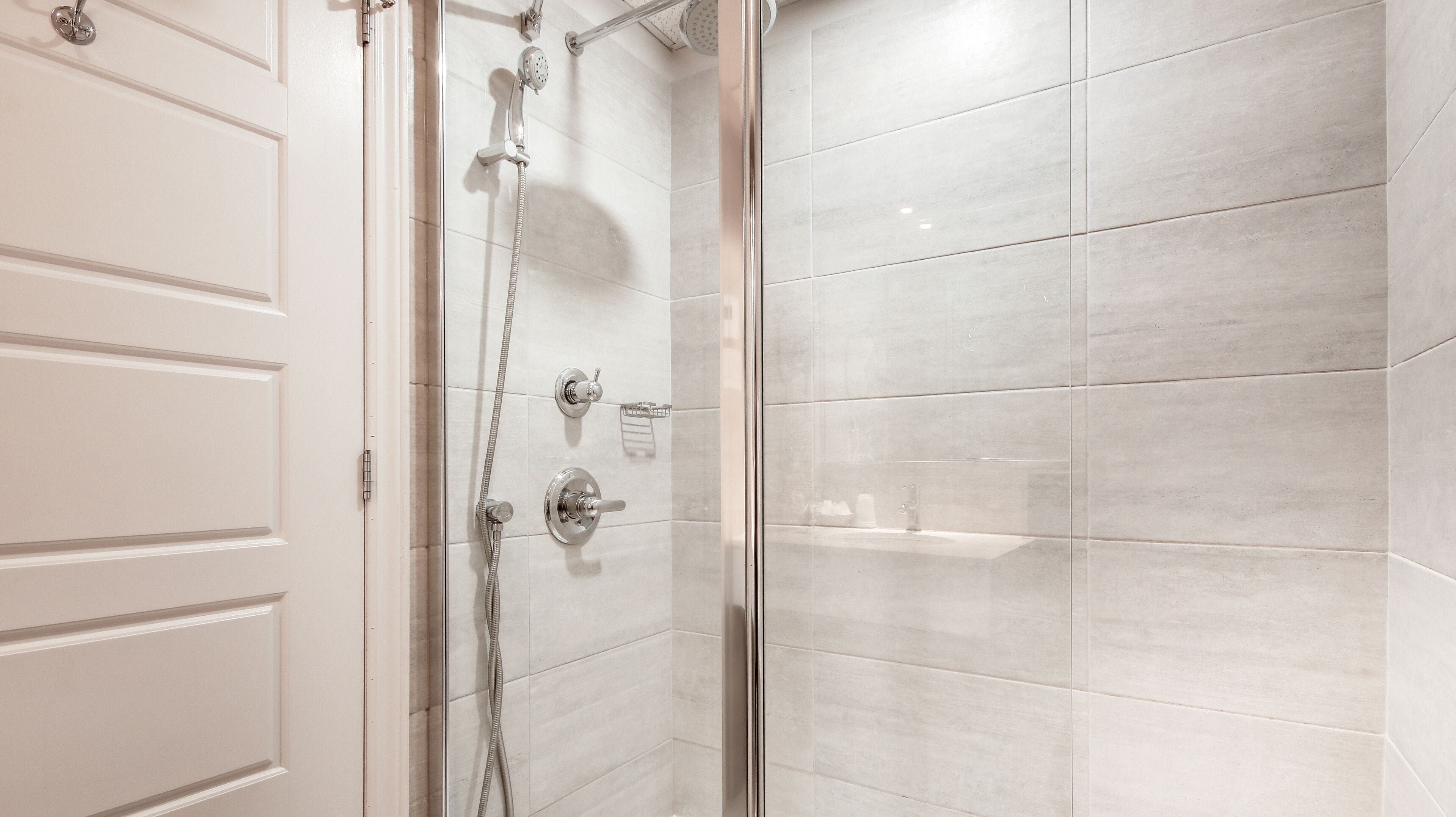 A modern bathroom with a glass shower enclosure, white tiled walls, and a white door.