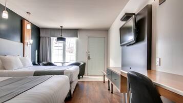 A hotel room with two beds, a desk, a chair, a TV, and a window with curtains.