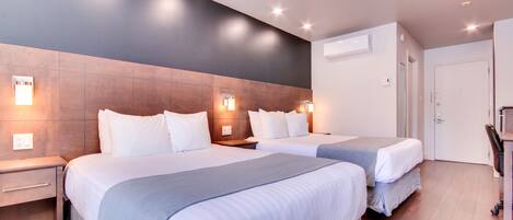 Ein Hotelzimmer mit zwei Betten, einem Holzkopfteil, Nachttischlampen, einem Schreibtisch und einem Stuhl.