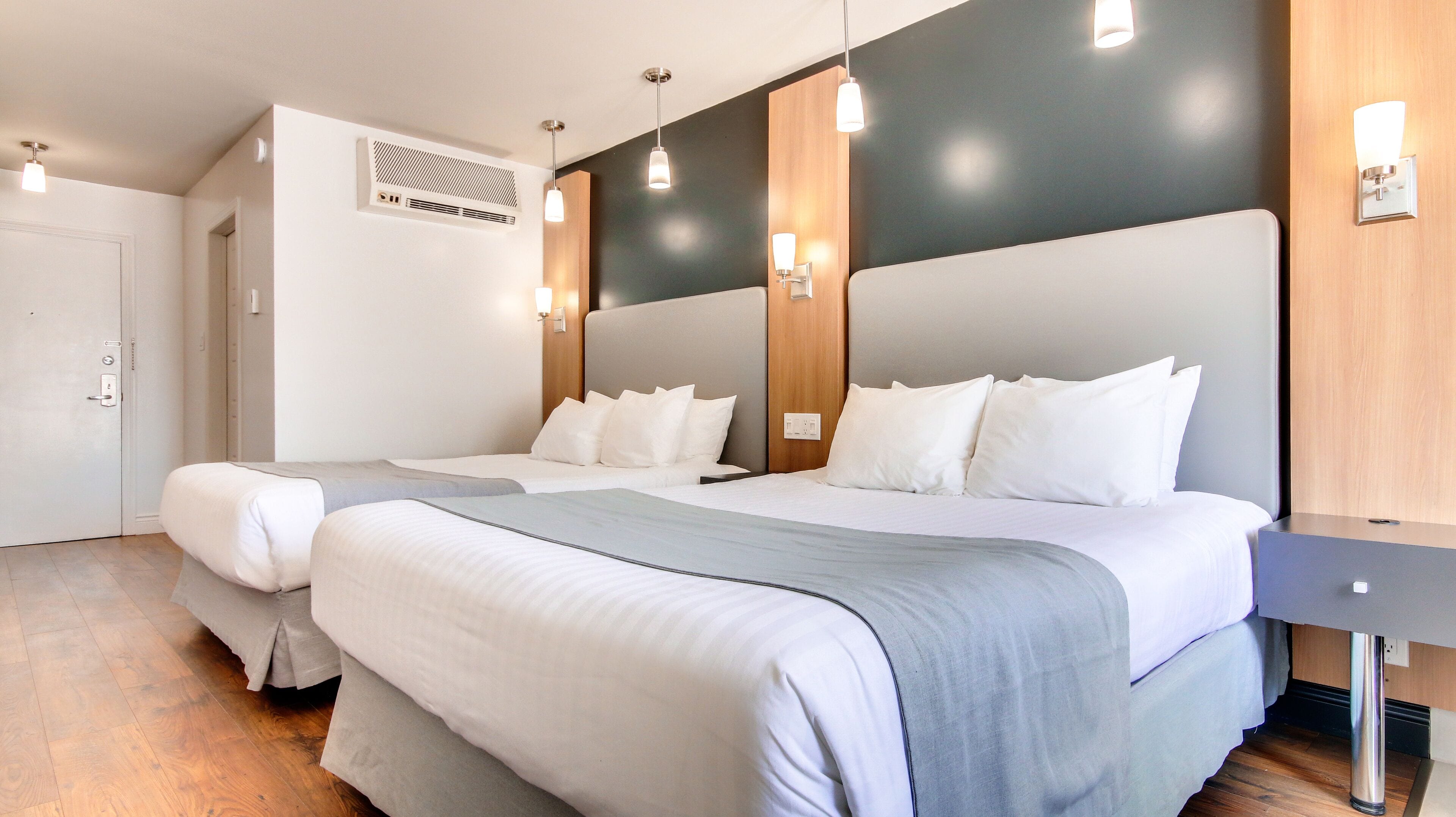Une chambre d’hôtel moderne avec deux lits, un mur décoratif en bois et des luminaires suspendus.