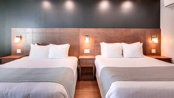 Una habitación de hotel con dos camas, cada una con una mesita de noche y una lámpara de pared.