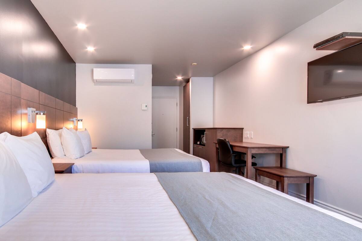 Una habitación de hotel con dos camas, un escritorio, una silla y un televisor.