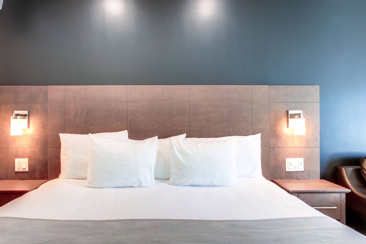 Una habitación de hotel moderna con una cama grande, dos mesitas de noche e iluminación en la pared.